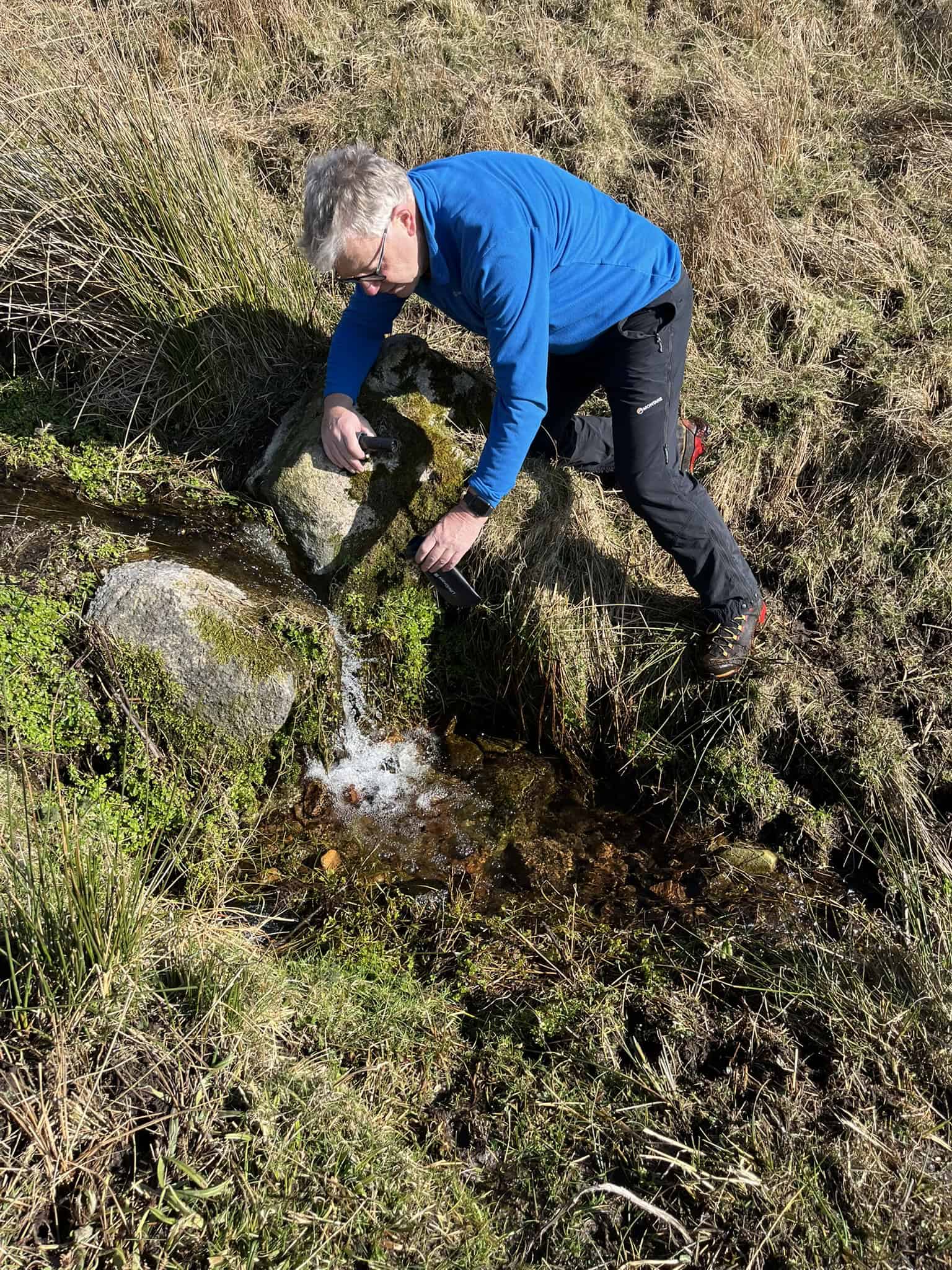 Collecting water from a mountain stream during a wild camping trip in the UK