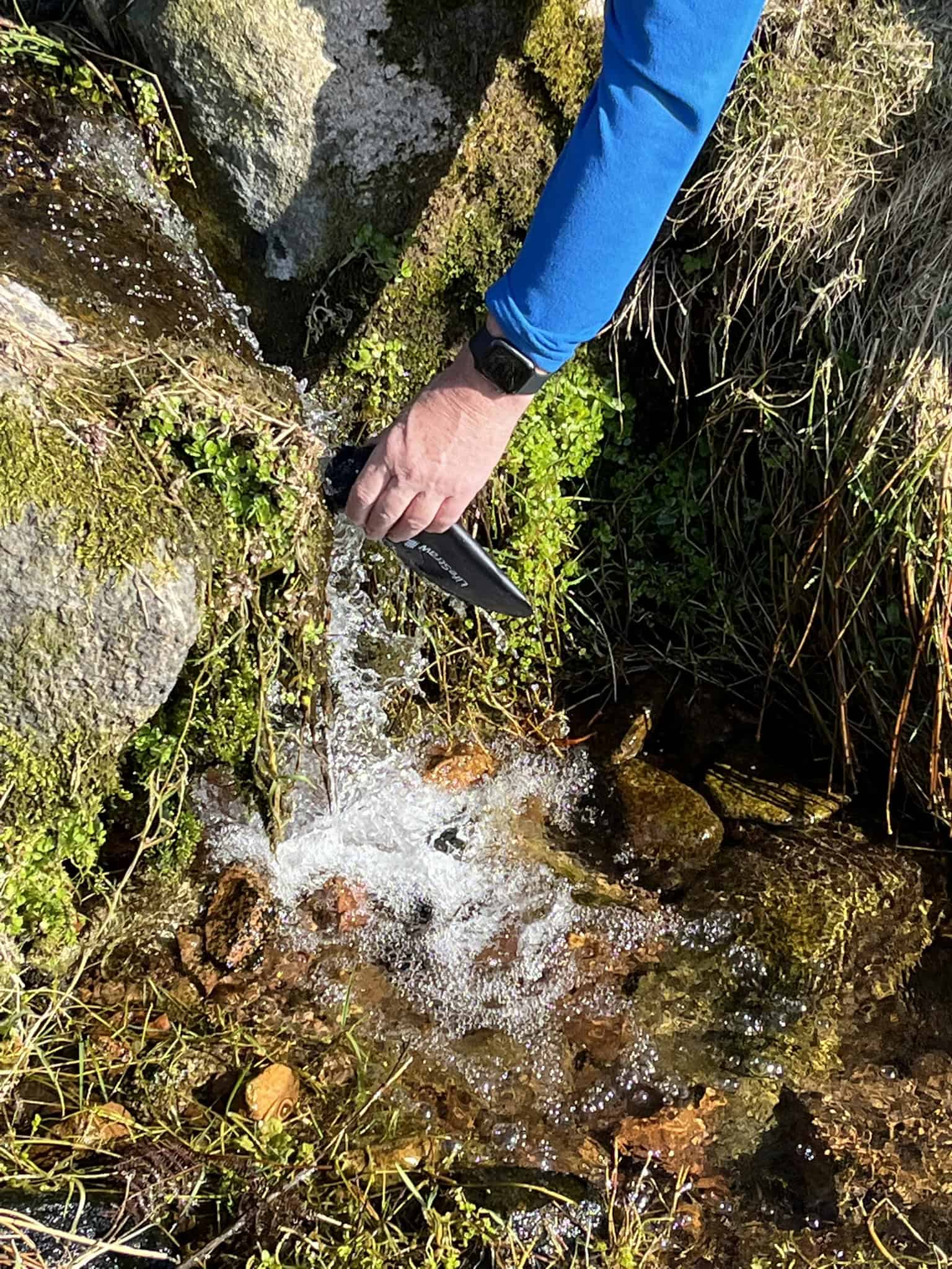 Using a portable water filter in a mountain stream while backpacking